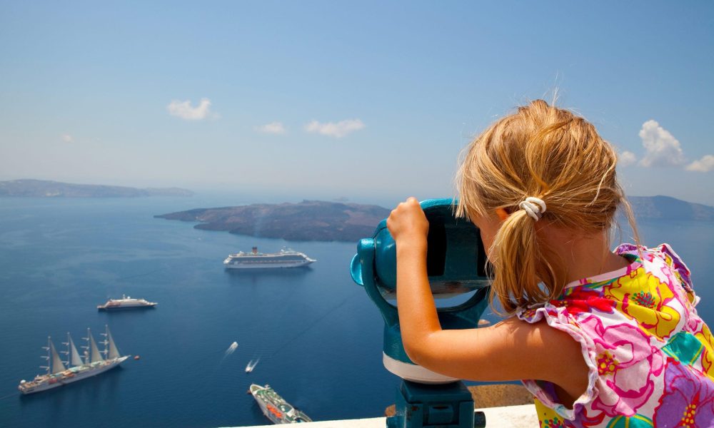 There are many interesting things to do in Santorini for families, like this girl checking out the volcano through a telescope from the caldera of Fira town.