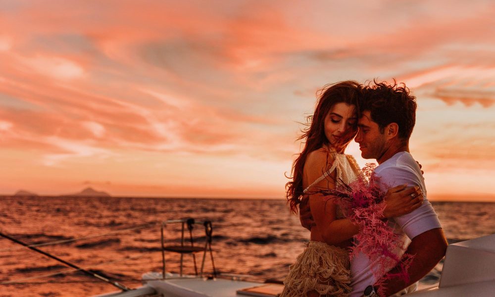 Couple embrace on a vessel at sea with the sunset sky background, enjoying a romantic dinner in Santorini.