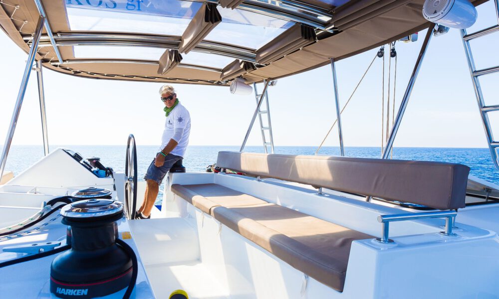 Captain Leo aboard a catamaran of the Spiridakos Sailing Cruises fleet, taking visitors on both private vs semi private cruises in Santorini.
