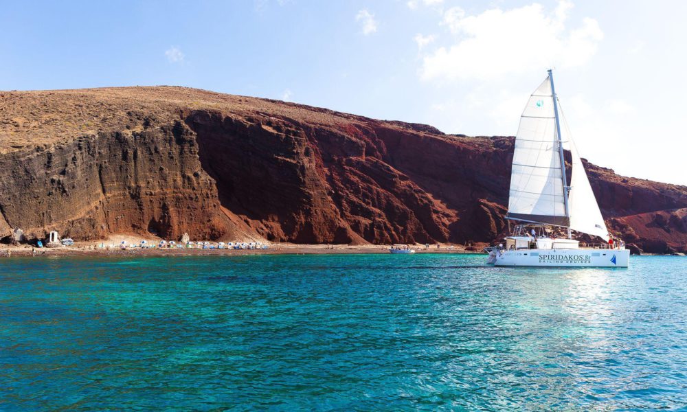 Spiridakos Sailing vessel at sea with the Red beach in the background during a Santorini catamaran tour