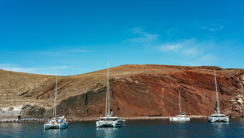 Catamarans anchored at the Red Beach, one of the popular stops on our Joy Daytime Santorini Half Day Cruise by Spiridakos Sailing Cruises.