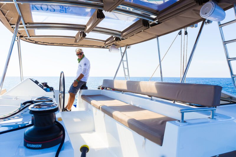 Captain Leo aboard a catamaran of the Spiridakos Sailing Cruises fleet, taking visitors on both private vs semi private cruises in Santorini.